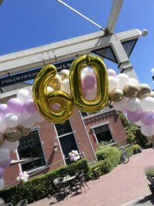 Ballonboog foliecijfers 60 met gouden, witte en lila ballonnen en Ballontrossen bij brug